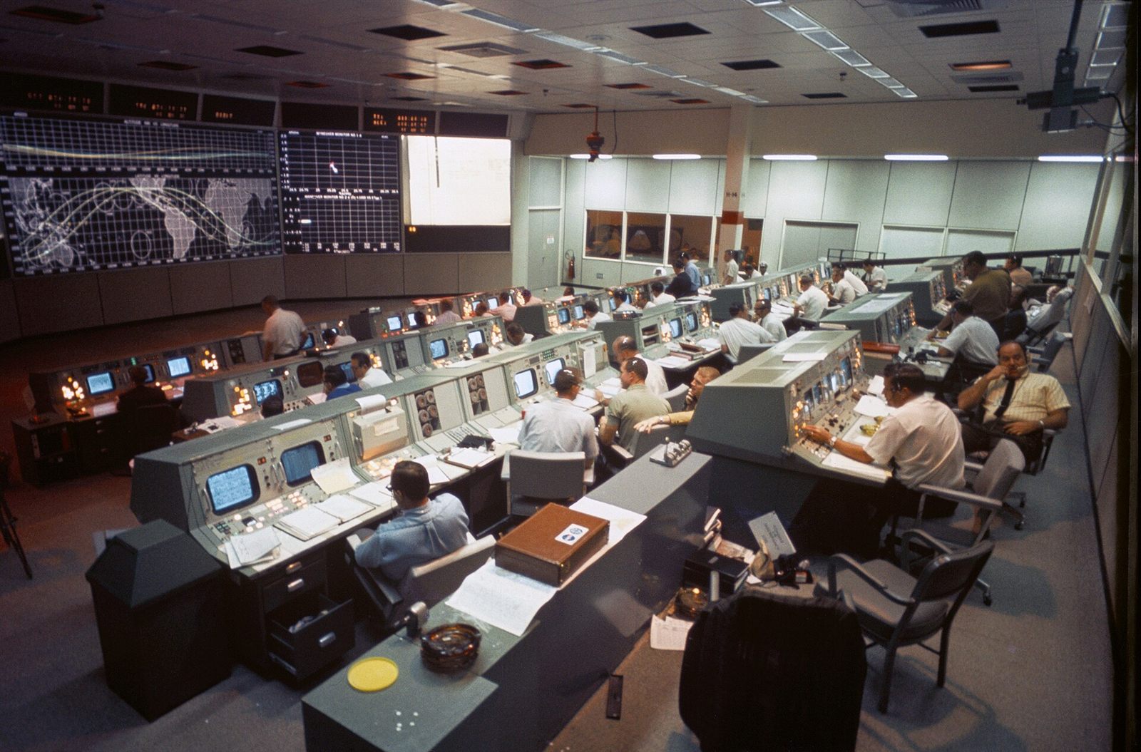 Sala de controle de missão da NASA em 1968, com fileiras de consoles e telões ao fundo