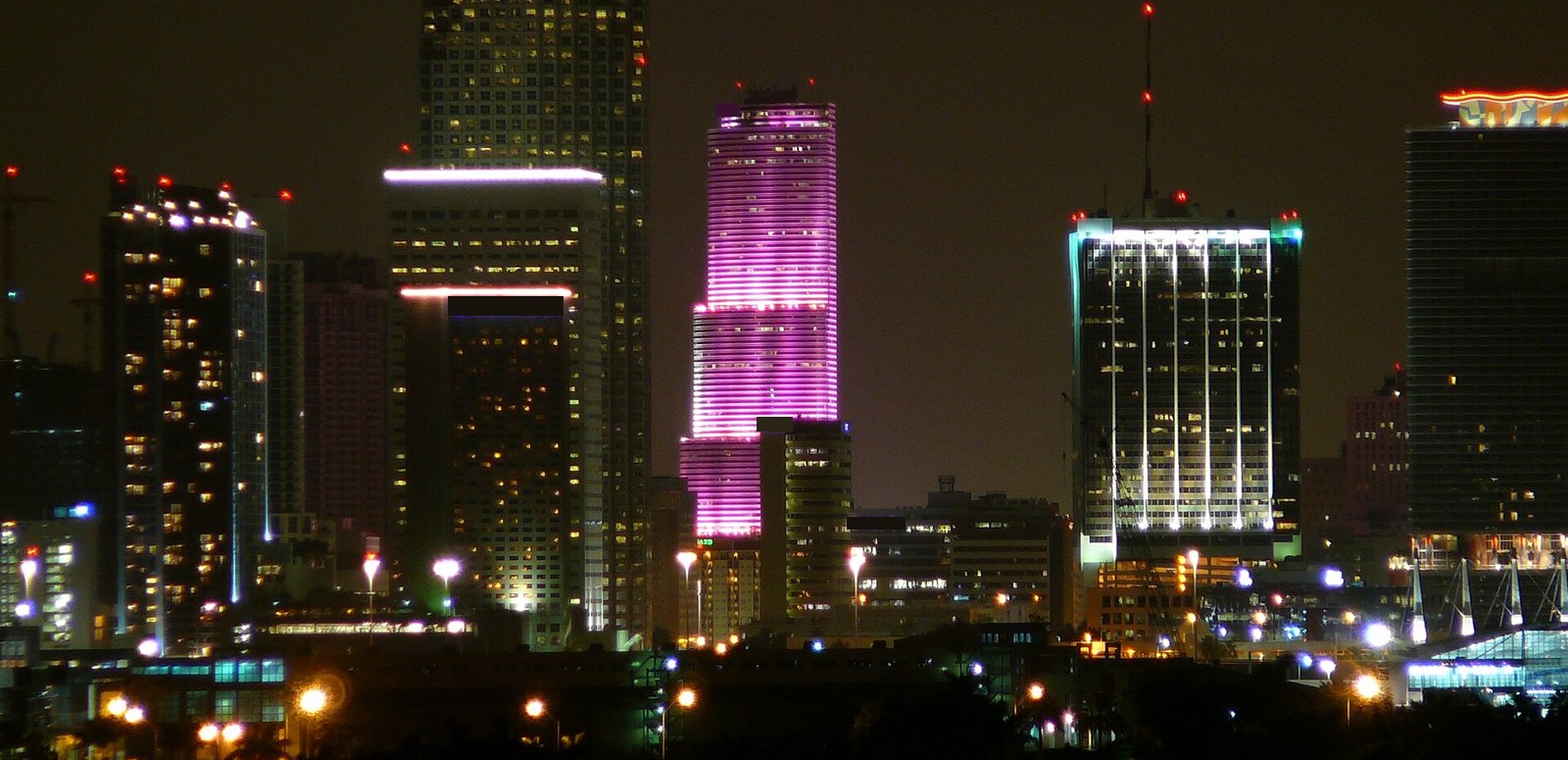 Prédios do centro de Miami à noite, com uma torre iluminada em rosa e violeta